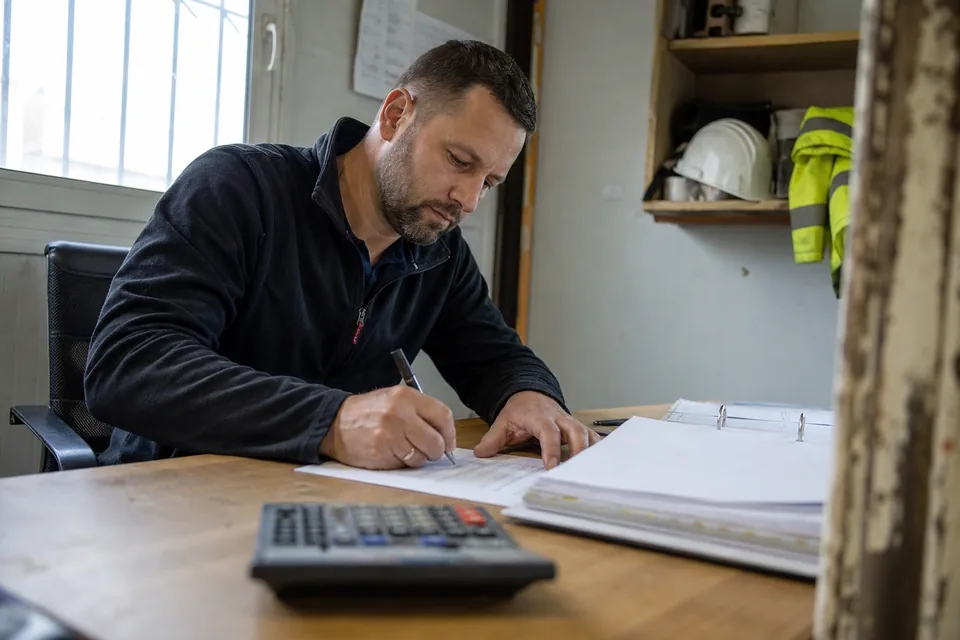 Właściciel firmy budowlanej podpisuje notę obciążeniową za odsetki przy biurku w biurze na budowie