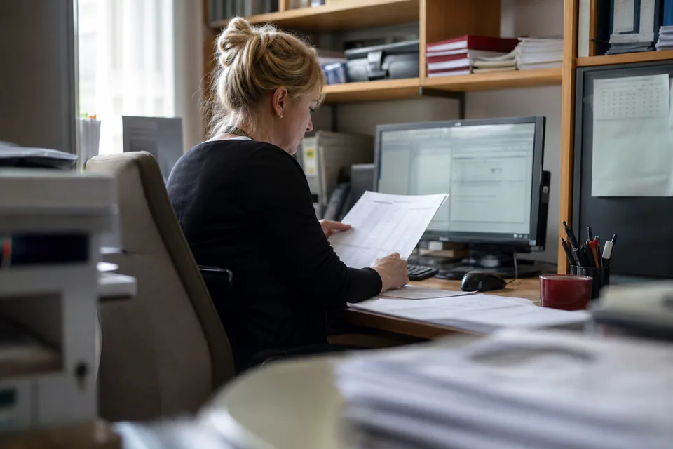 Księgowa w biurze rachunkowym porównuje zestawienie faktur z ekranem programu