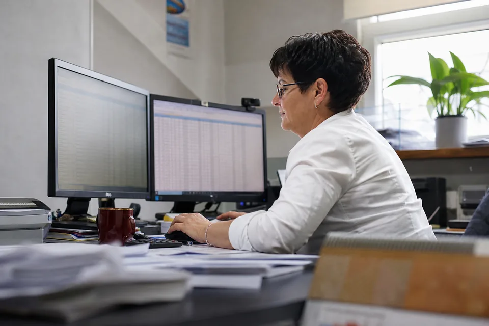 Księgowa przy dwóch monitorach z tabelą faktur do korekty VAT